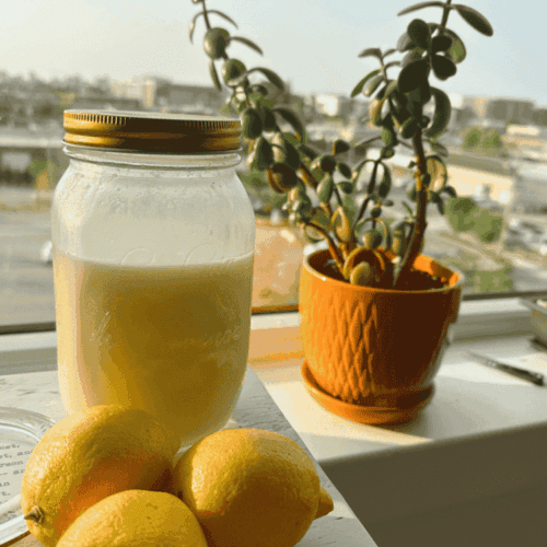 Lemon olive oil elixir sitting on window sill with lemons in front of a jade plant