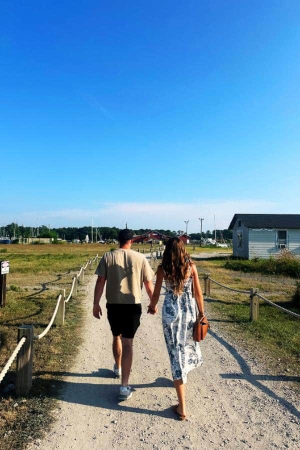 Romantic couple strolling along a summery coastal path in Cape Charles, Virginia, on a sunny birthday weekend.