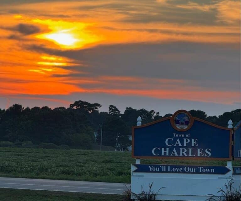 Scenic sunset over Cape Charles with vibrant orange and yellow skies, welcoming town sign in the foreground.